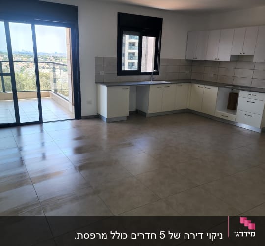 רצפה נקייה במטבח ריק עם ארונות לבנים וחלון גדול